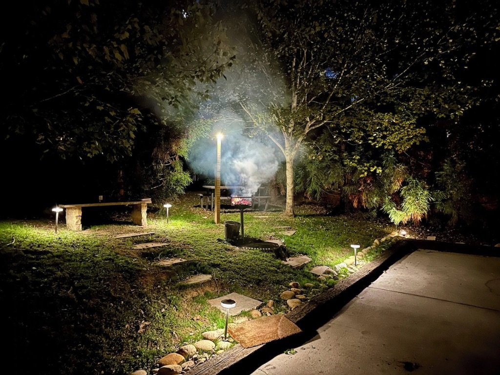 Pigeon Hills backyard at night with fire pit stone pathways ambient lighting and forest backdrop