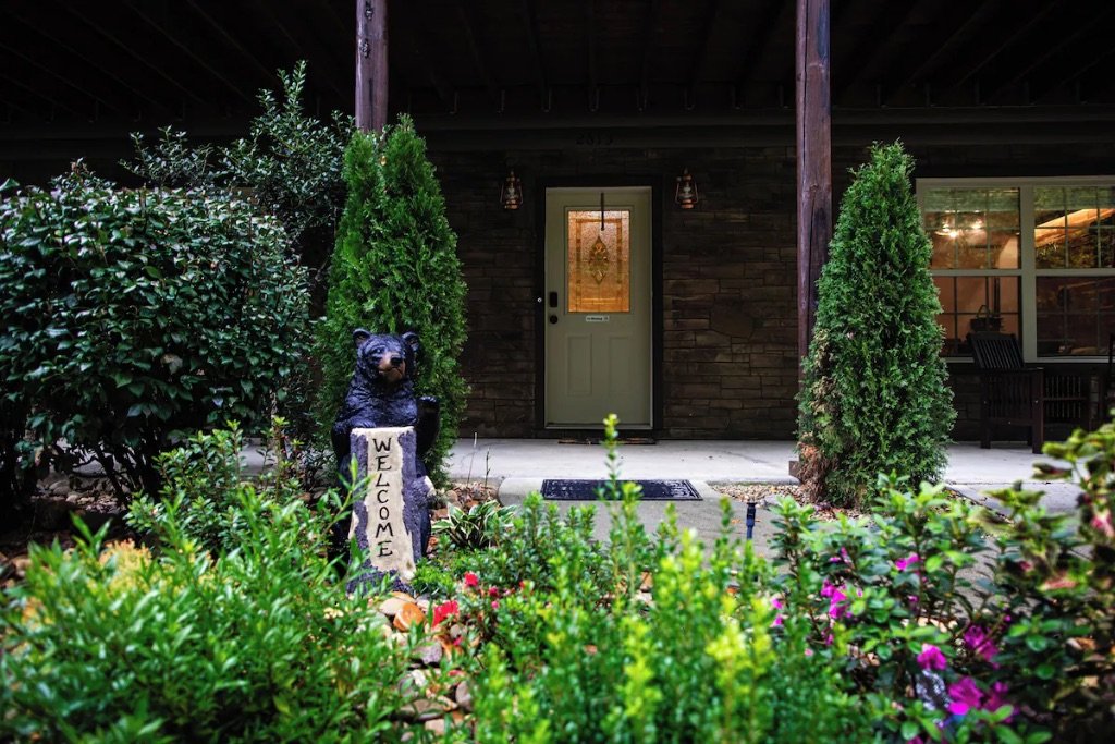 Pigeon Hills cabin entrance at night with bear welcome statue landscape lighting and garden