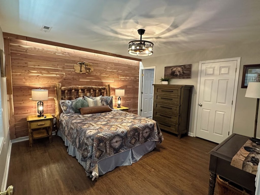 Pigeon Hills master bedroom angle view with king bed wood paneling ceiling fan and mountain decor